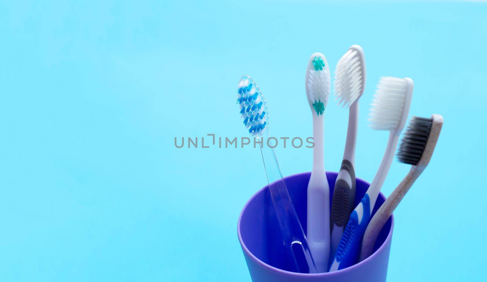 Toothbrushes in plastic glass on blue background. Copy space by Bowonpat