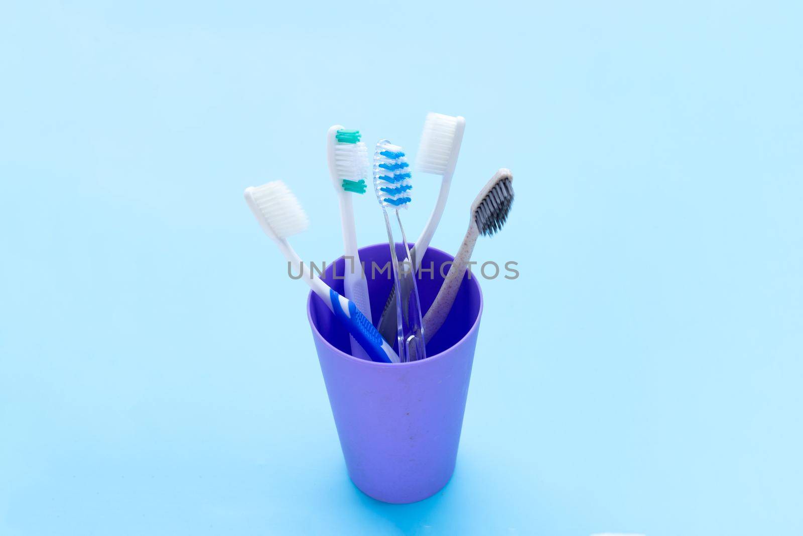 Toothbrushes in plastic glass on blue background. Copy space