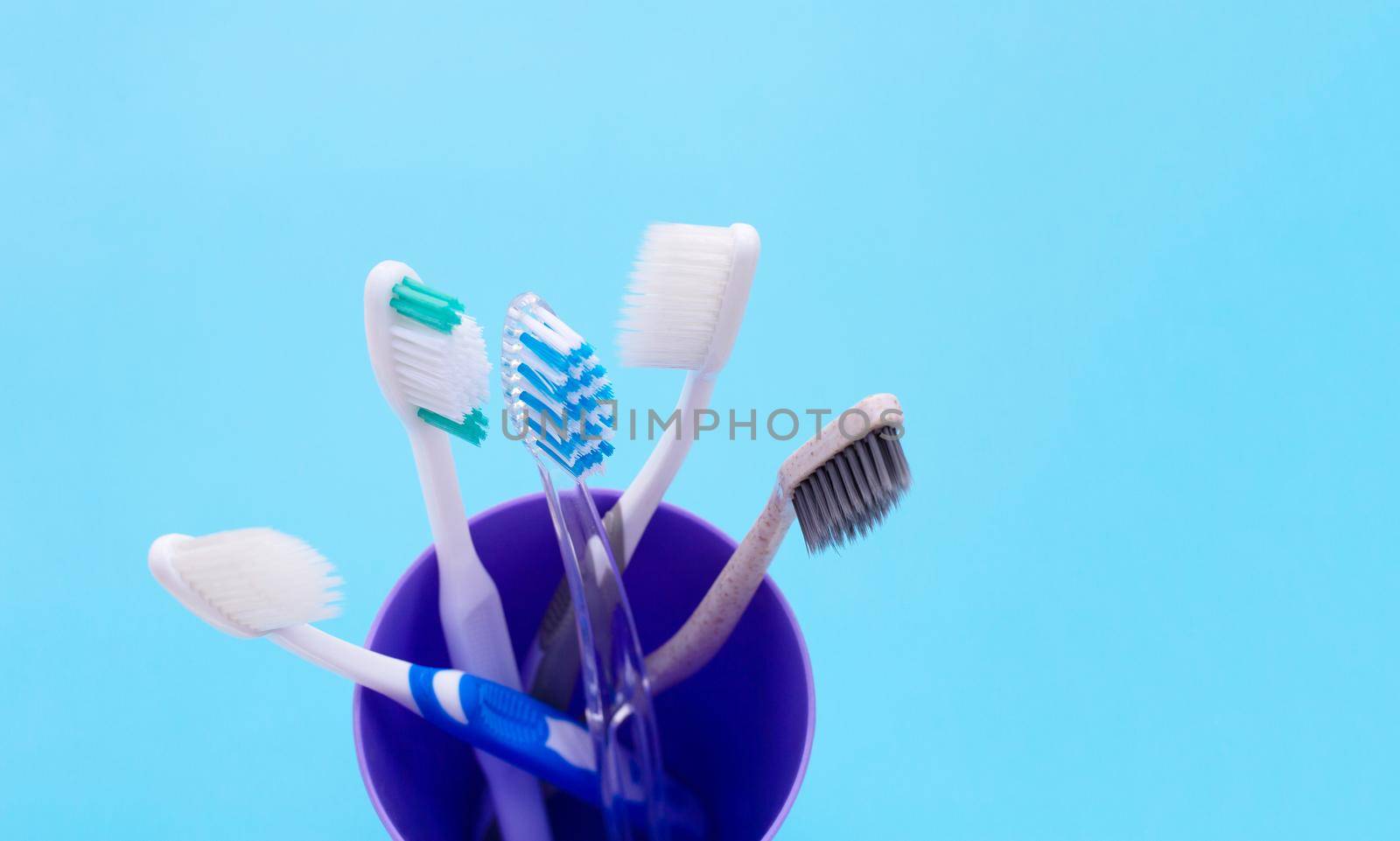 Toothbrushes in plastic glass on blue background. Copy space