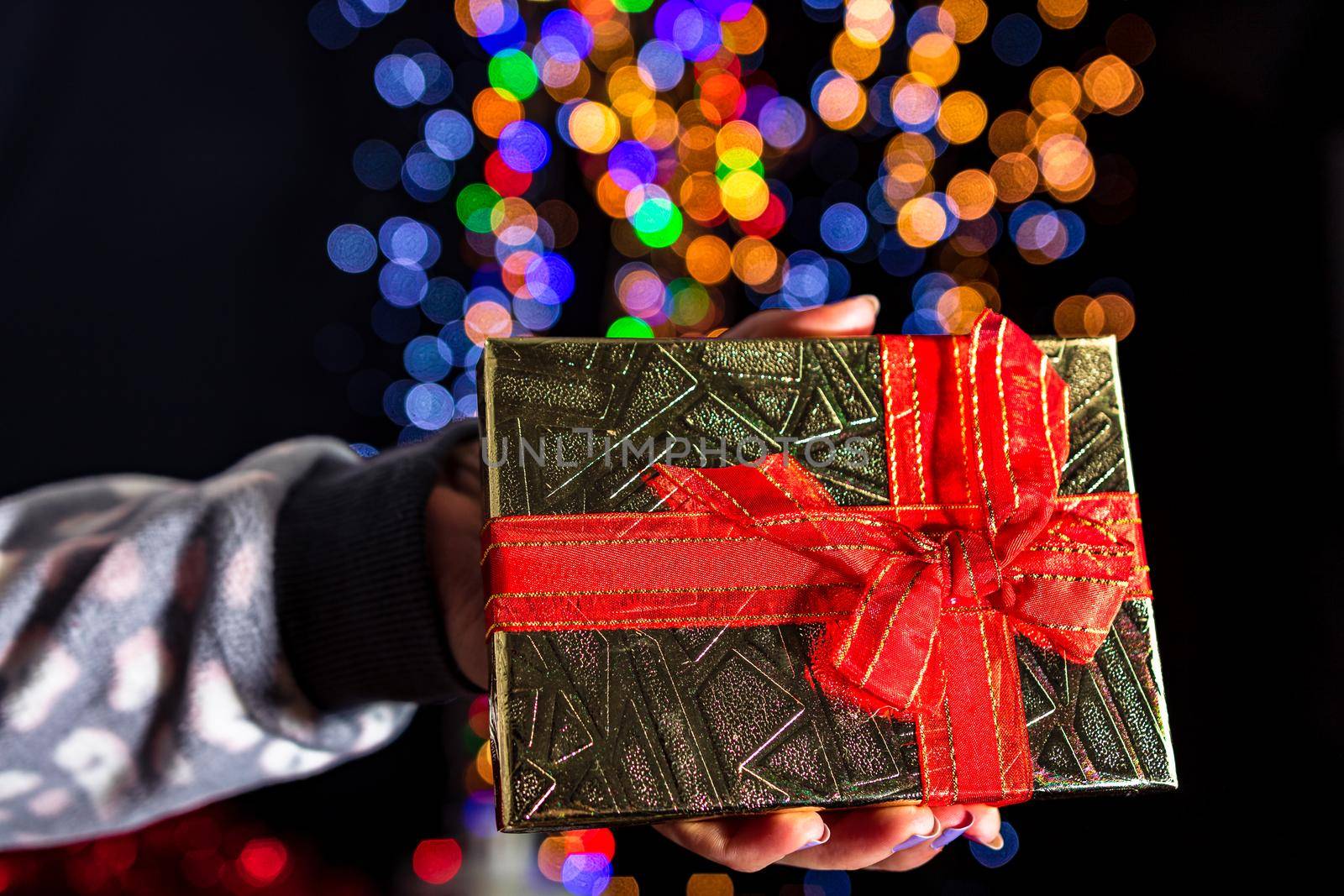 Holding Christmas gift isolated on background with blurred lights. December season, Christmas composition.