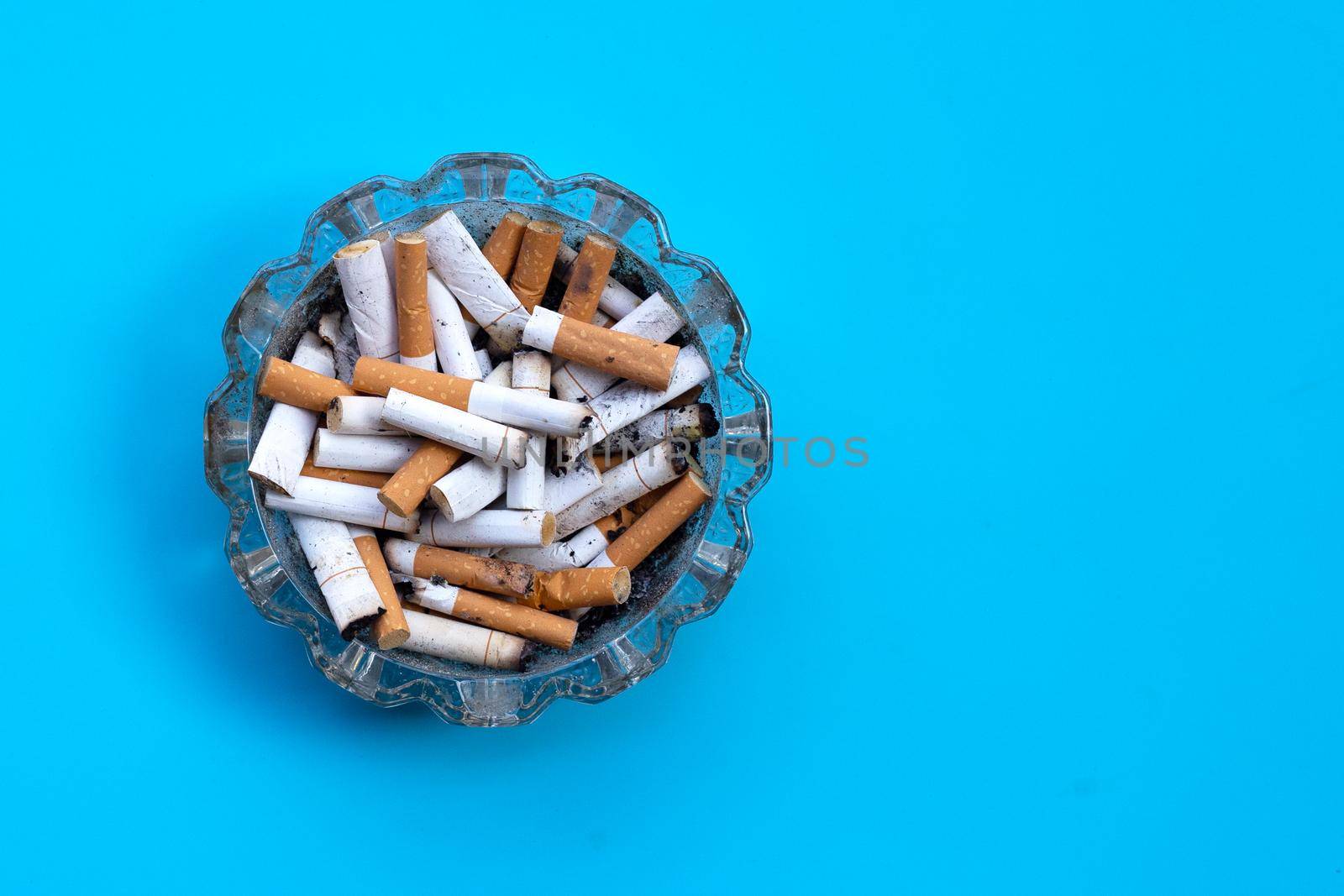 Cigarettes buds in a transparent ashtray on blue background.
