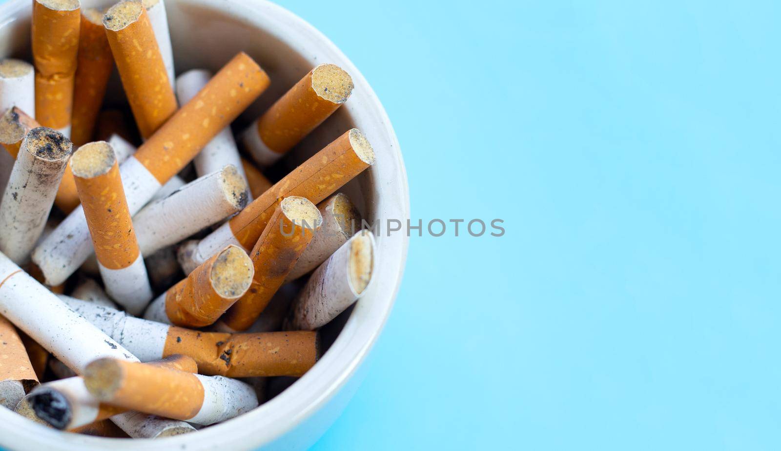 Cigarettes buds in a transparent ashtray on  blue background. Copy space