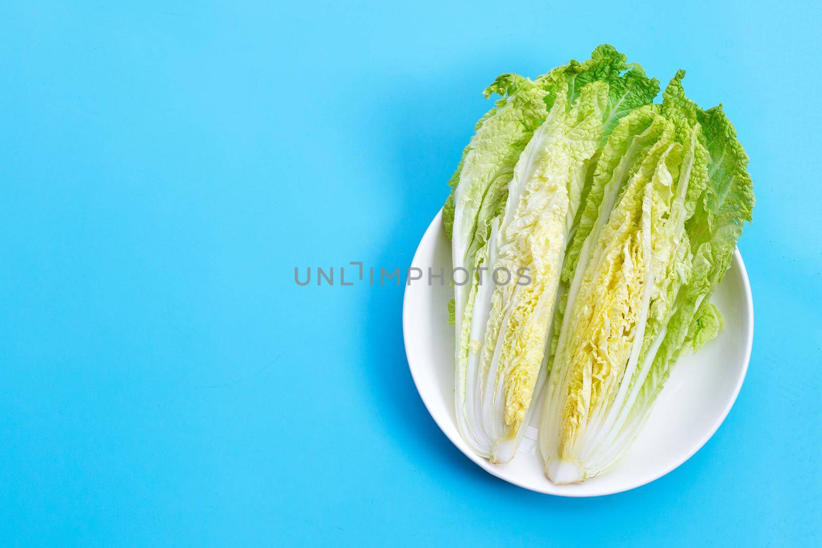 Chinese cabbage cut on  white plate on blue background. Top view