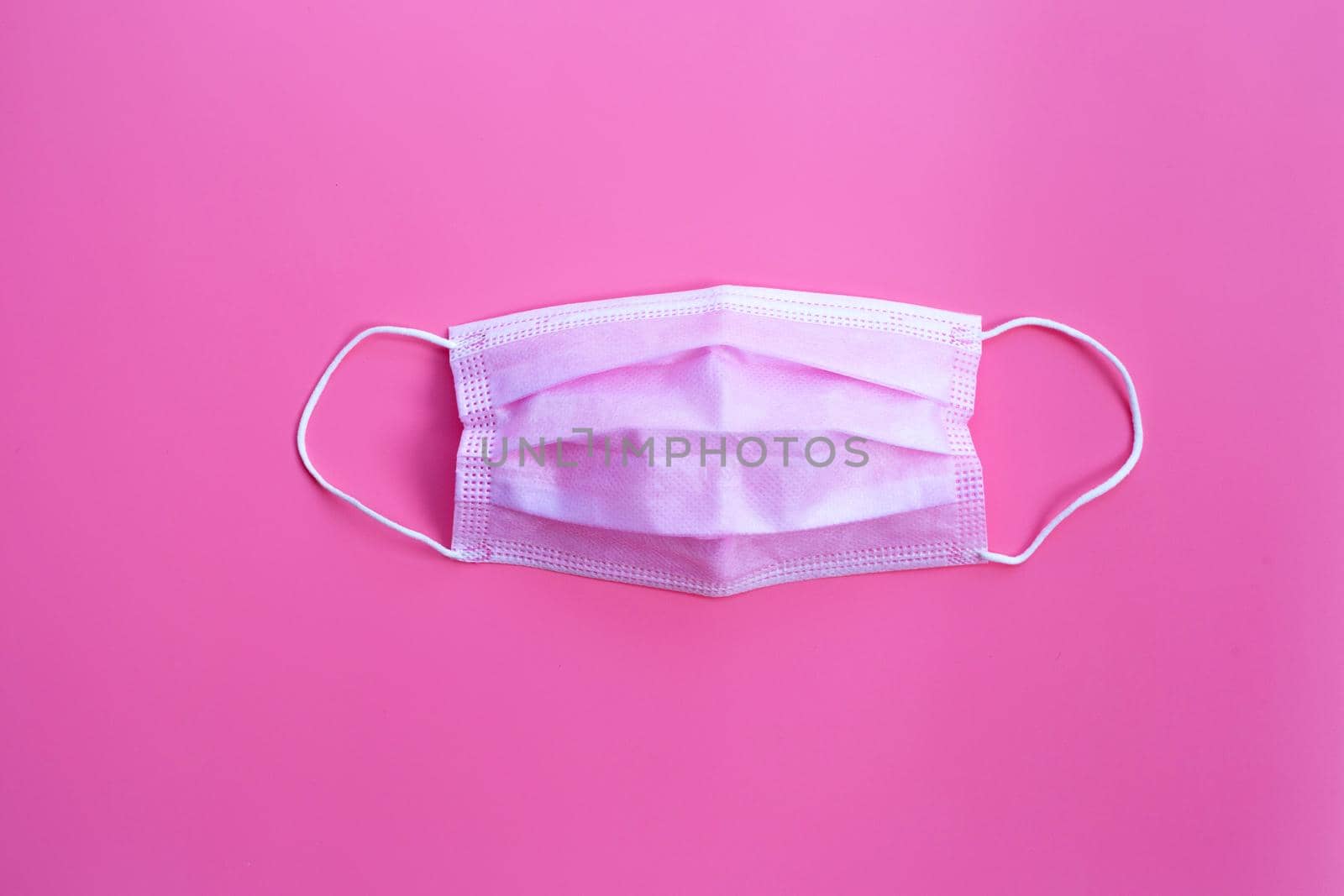 Pink protective medical mask on pink background. Top view
