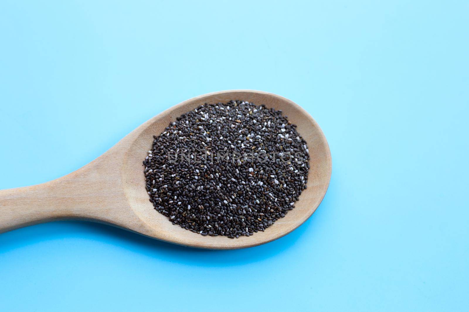 Chia seeds in a wooden spoon on blue background.