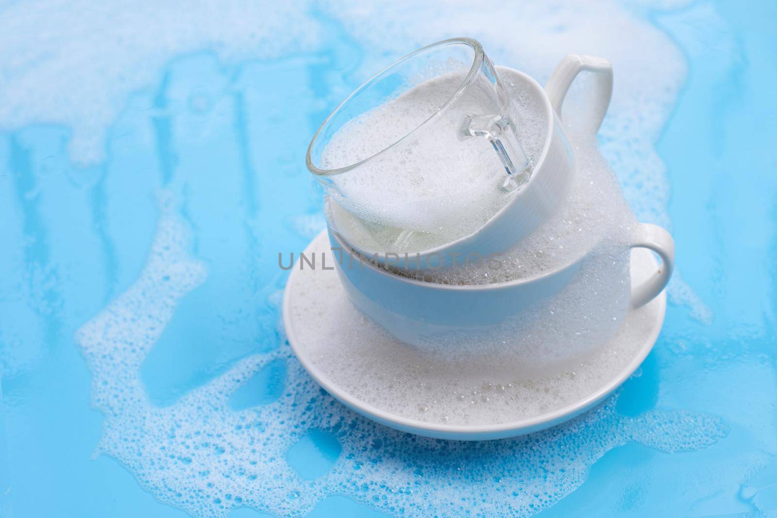 Washing an used drinking cups on wet blue with soapy foam background.
