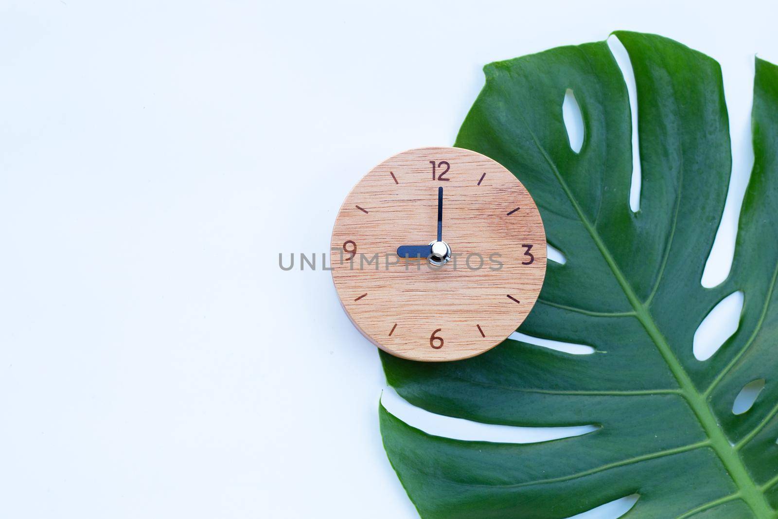 Wooden clock on green leaves on white background. Copy space by Bowonpat