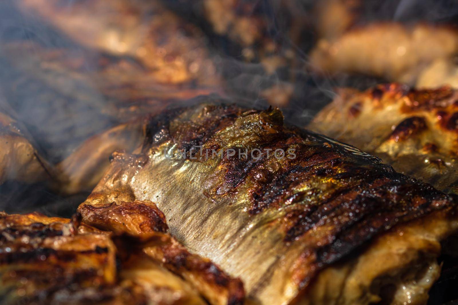 Grilled mackerel fish with smoke on a charcoal barbecue grill.