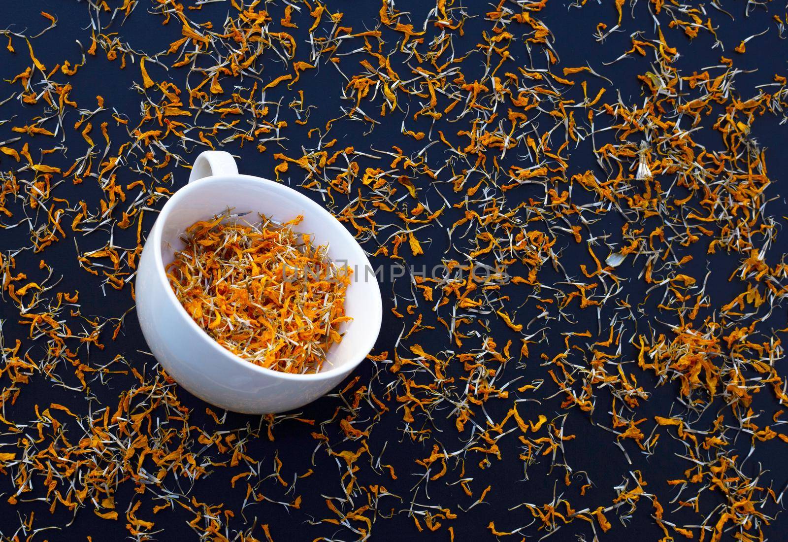 White cup with dry marigold flower petals on dark background. Herbal tea concept. by Bowonpat