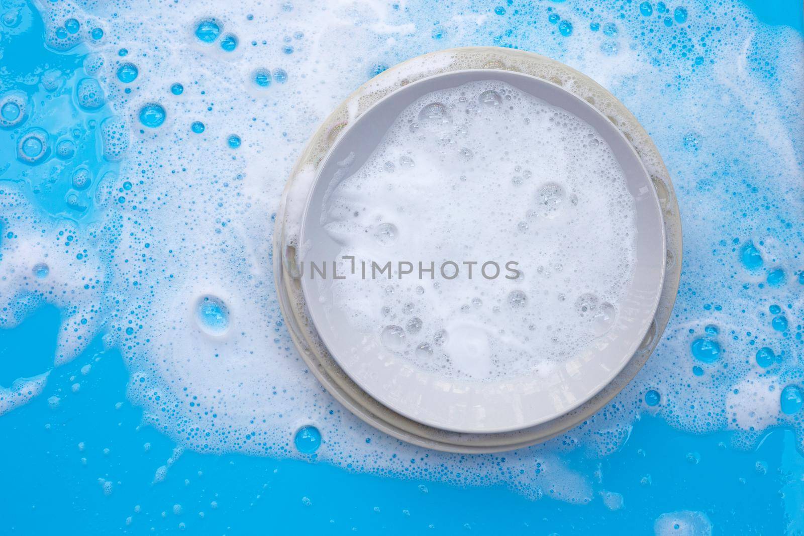 Washing dishes on wet blue background with soapy foam.