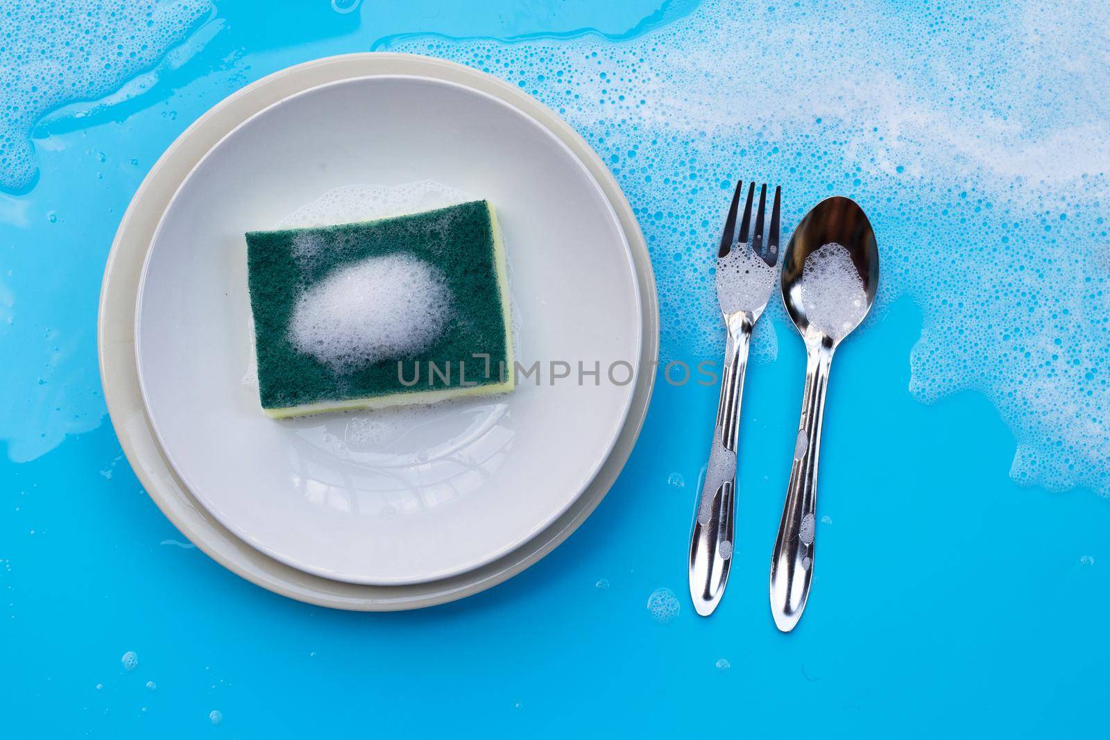 Washing dishes on wet blue background with soapy foam. by Bowonpat