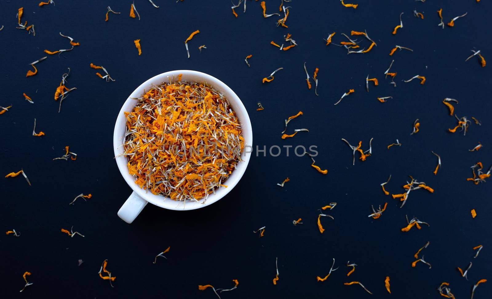 White cup with dry marigold flower petals on dark background. Herbal tea concept. by Bowonpat