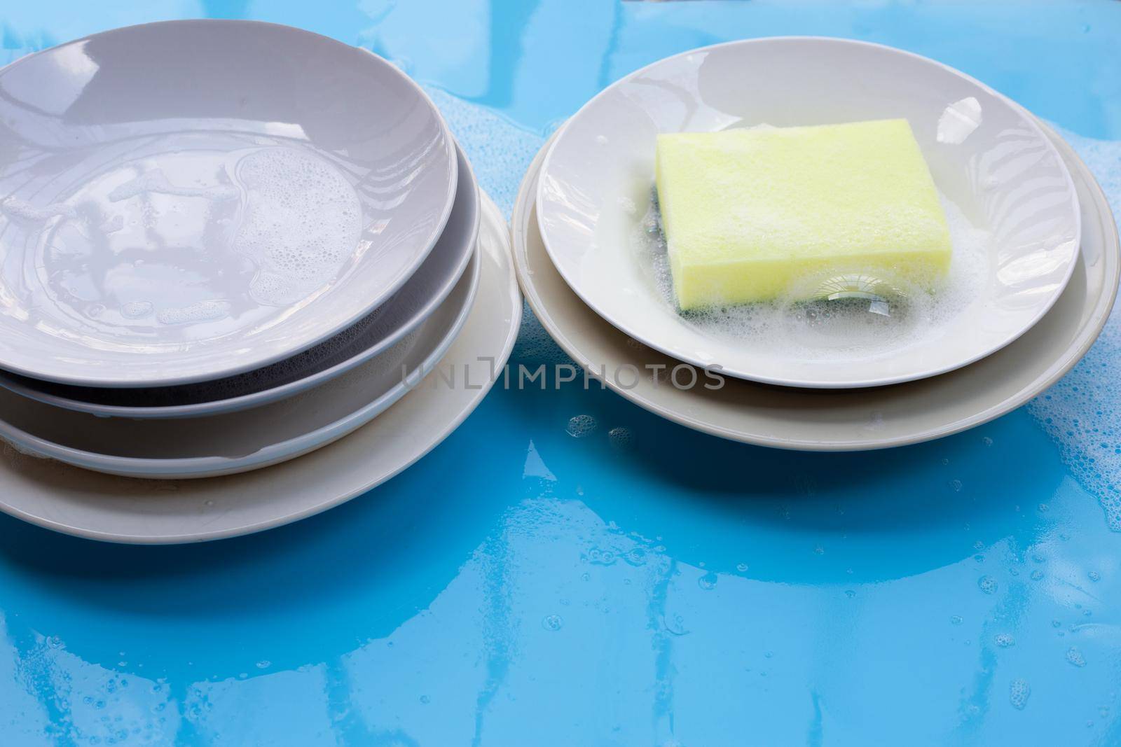 Washing dishes on wet blue background with soapy foam. by Bowonpat
