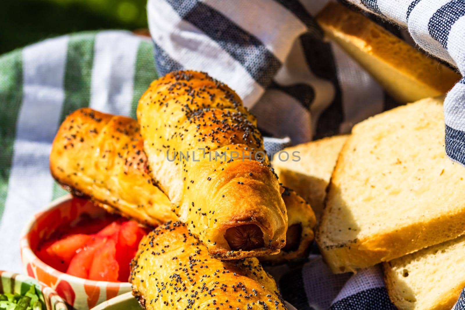 Sausages baked in dough sprinkled with salt and poppy seeds in a rustic composition. Sausages rolls, delicious homemade pastries.