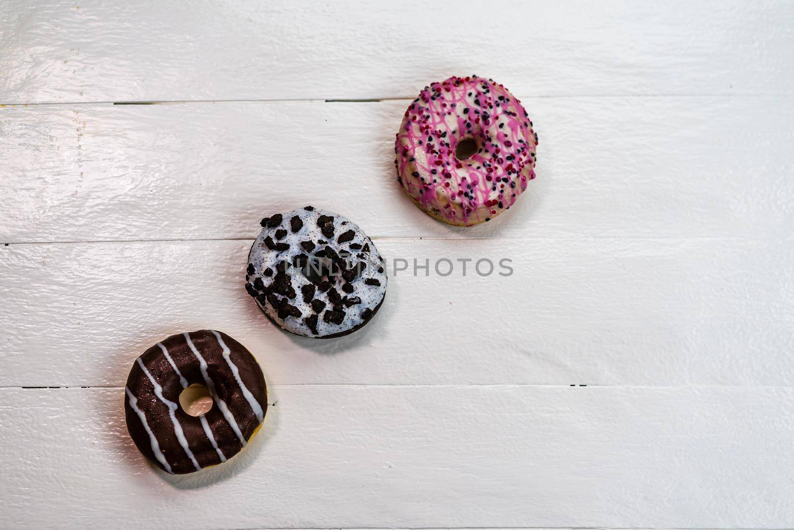 Colorful donuts on white wooden table. Sweet icing sugar food with glazed sprinkles, doughnut with frosting. Top view with copy space