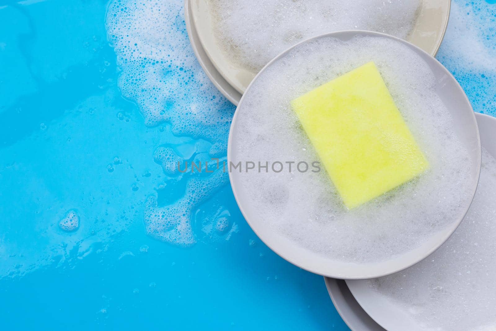Washing dishes concept. wet blue with soapy foam background.