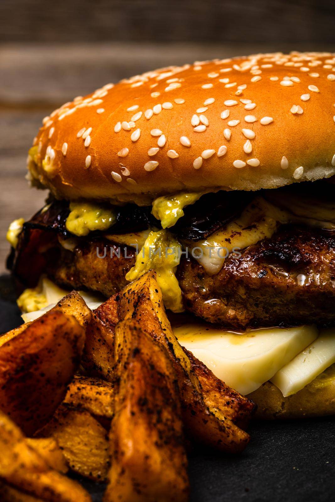 Detail view of fresh tasty cheese burger and fried potatoes on a wooden table