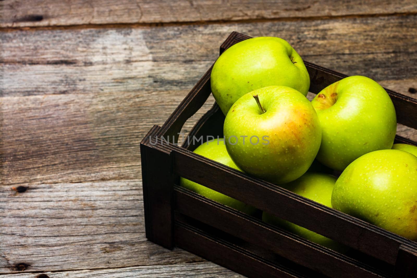 Wooden crate with ripe green apples on wooden table. by vladispas