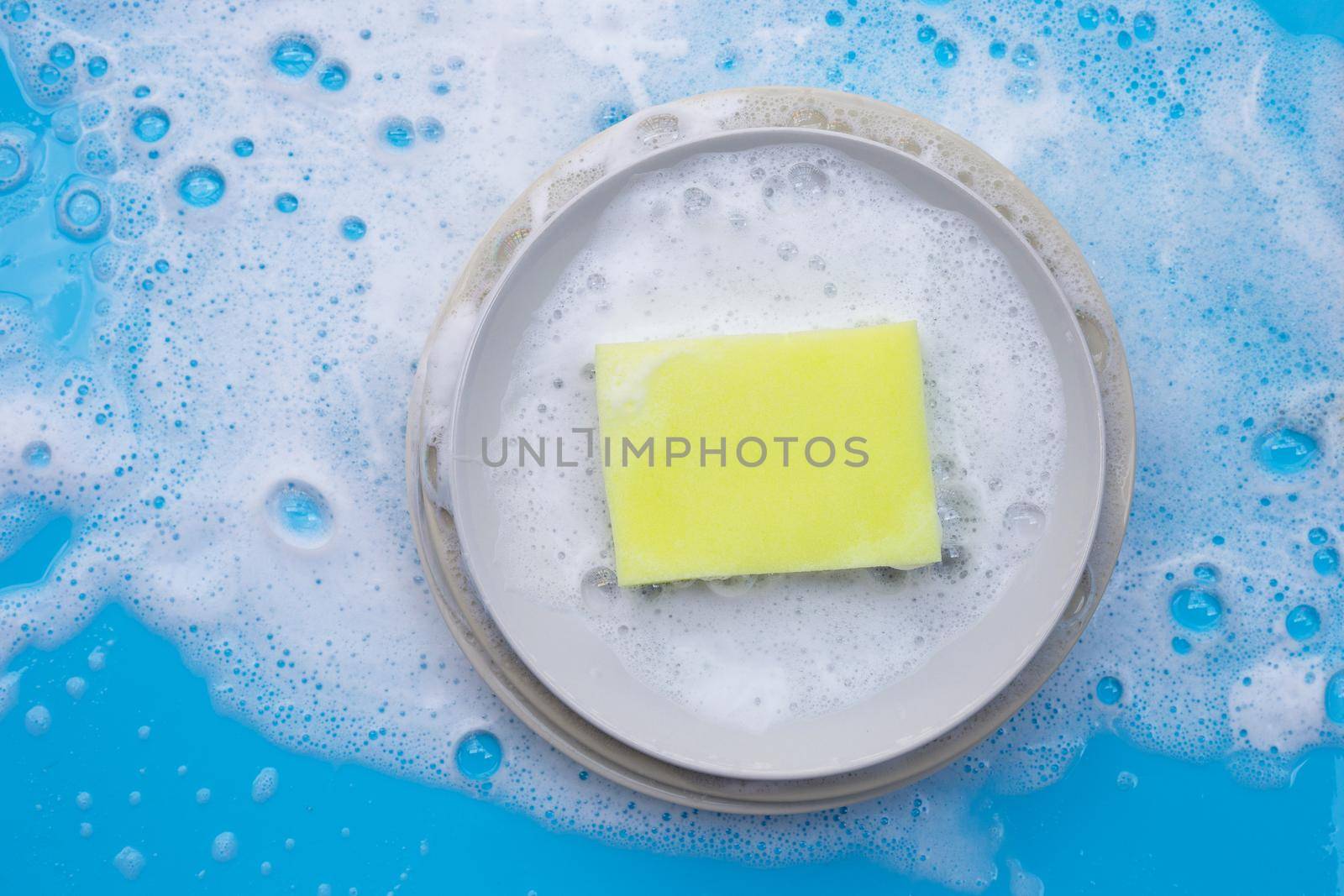 Washing dishes on wet blue background with soapy foam. by Bowonpat