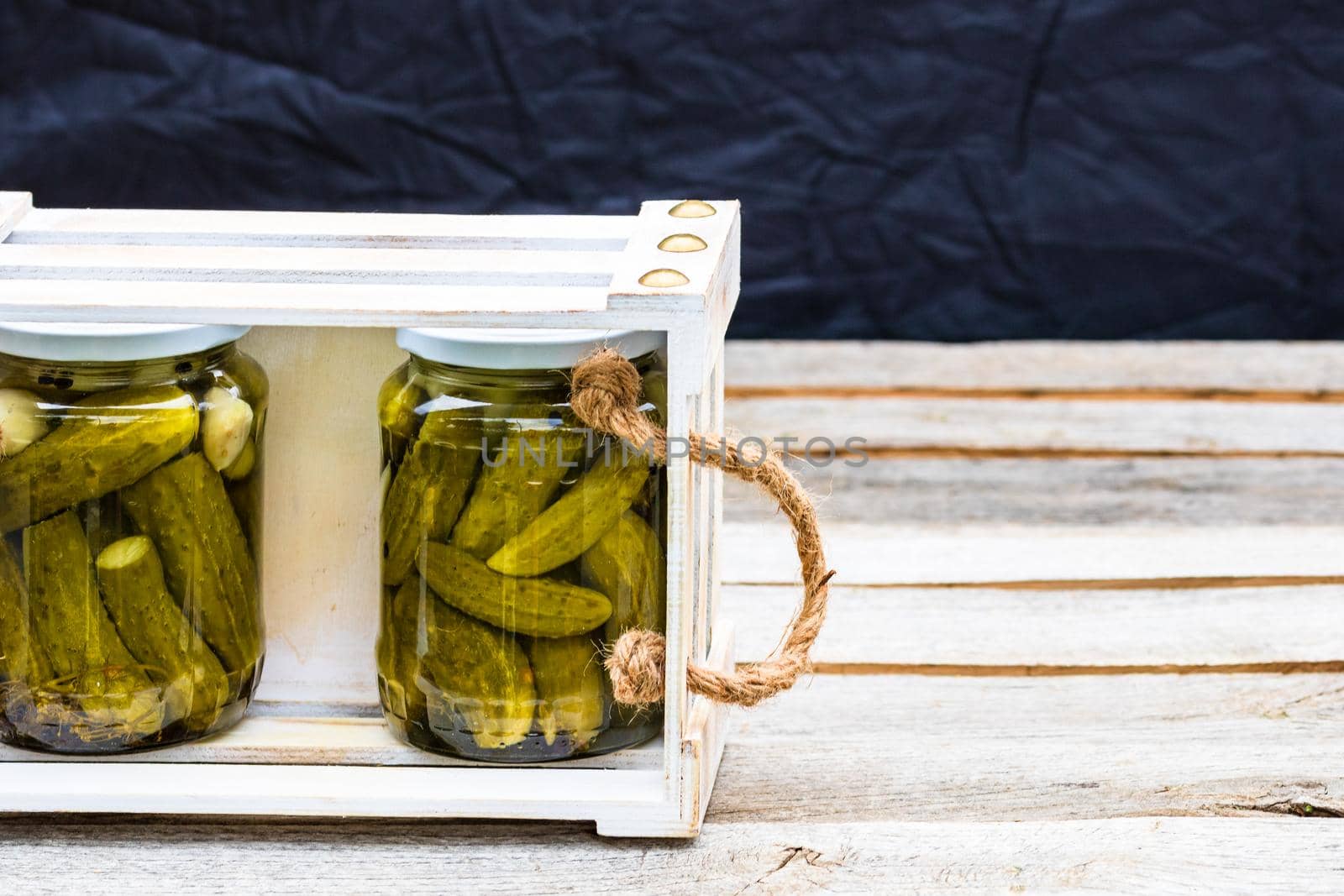 Wooden crate with glass jars with pickles isolated. Preserved food concept, canned vegetables isolated in a rustic composition. by vladispas