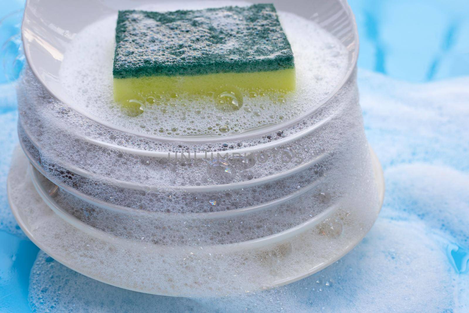 Washing dishes concept. wet blue with soapy foam background.