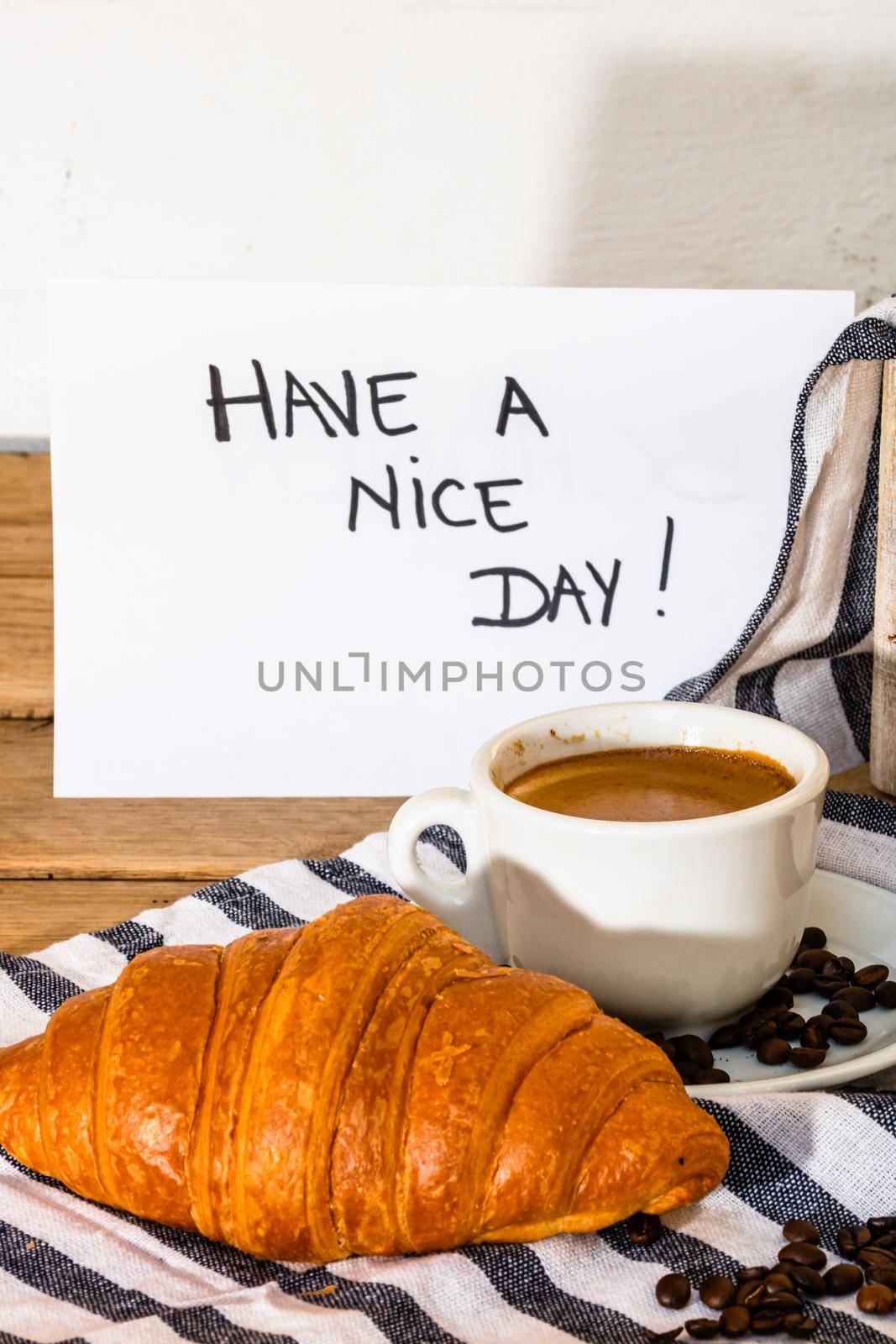 Coffee cup and buttered fresh French croissant on wooden crate. Food and breakfast concept. Morning message “have a nice day” o white board