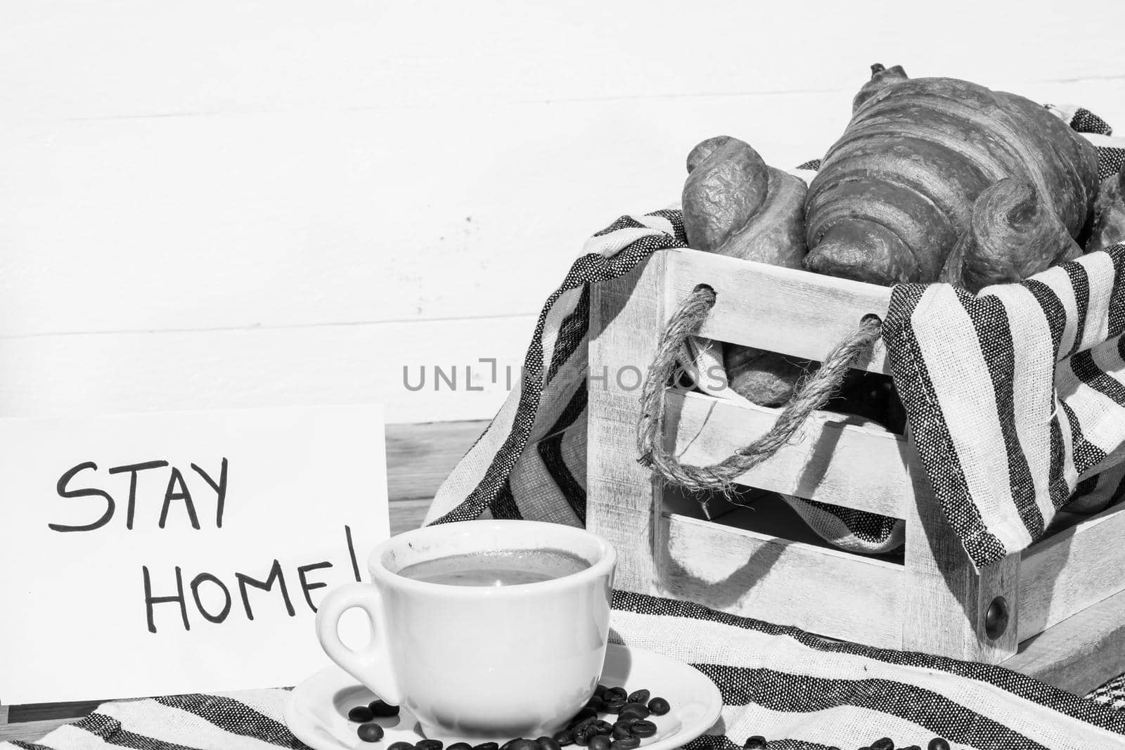 Coffee cup and buttered fresh French croissant on wooden crate. Food and breakfast concept. Morning message “stay home” on white board by vladispas