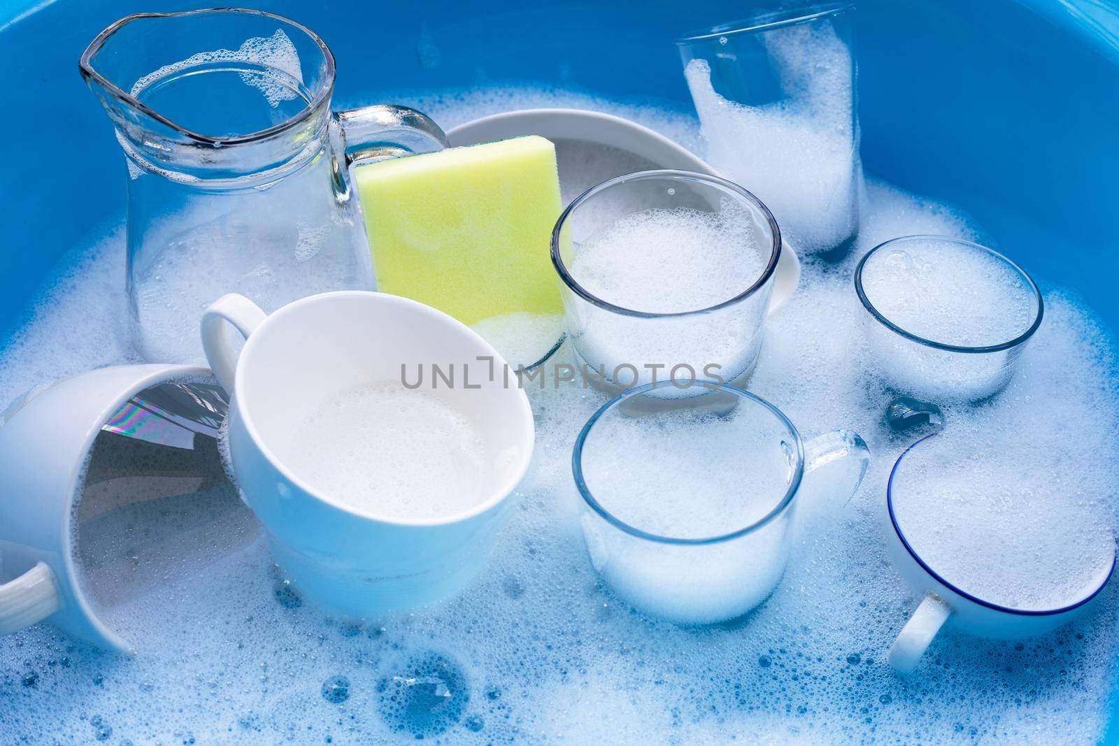 Washing used drinking glasses and cups with yellow sponge