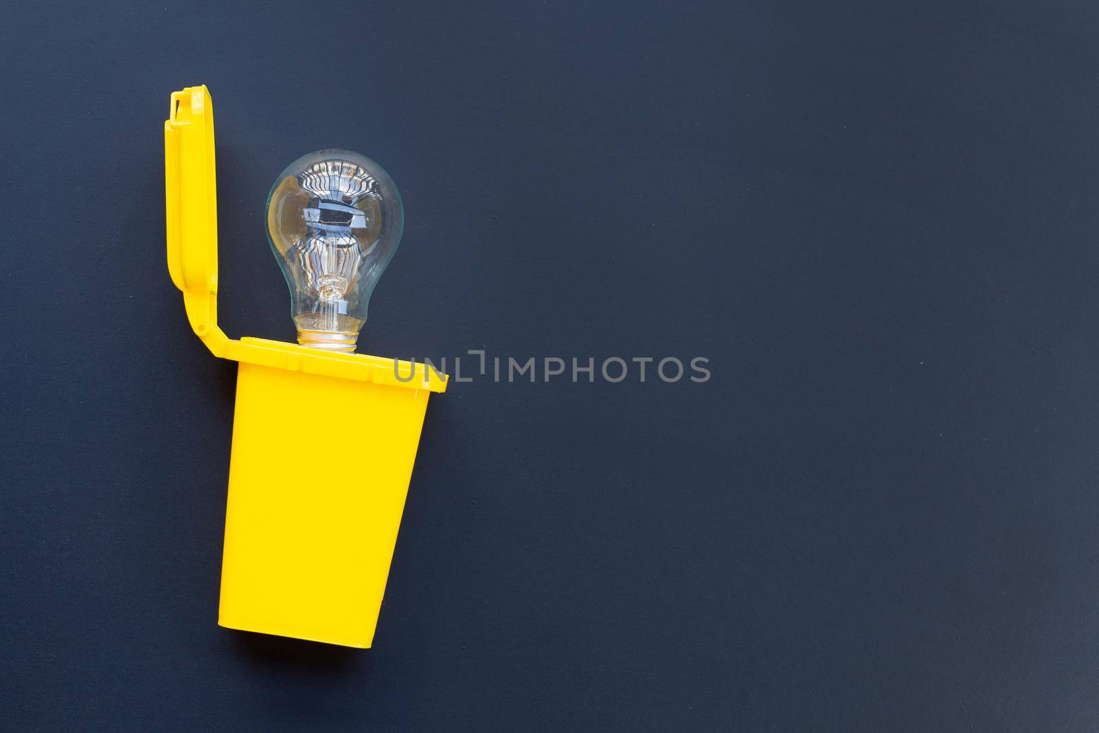 Yellow bin with light bulb on dark background. Ideas and creative thinking concept. Top view by Bowonpat