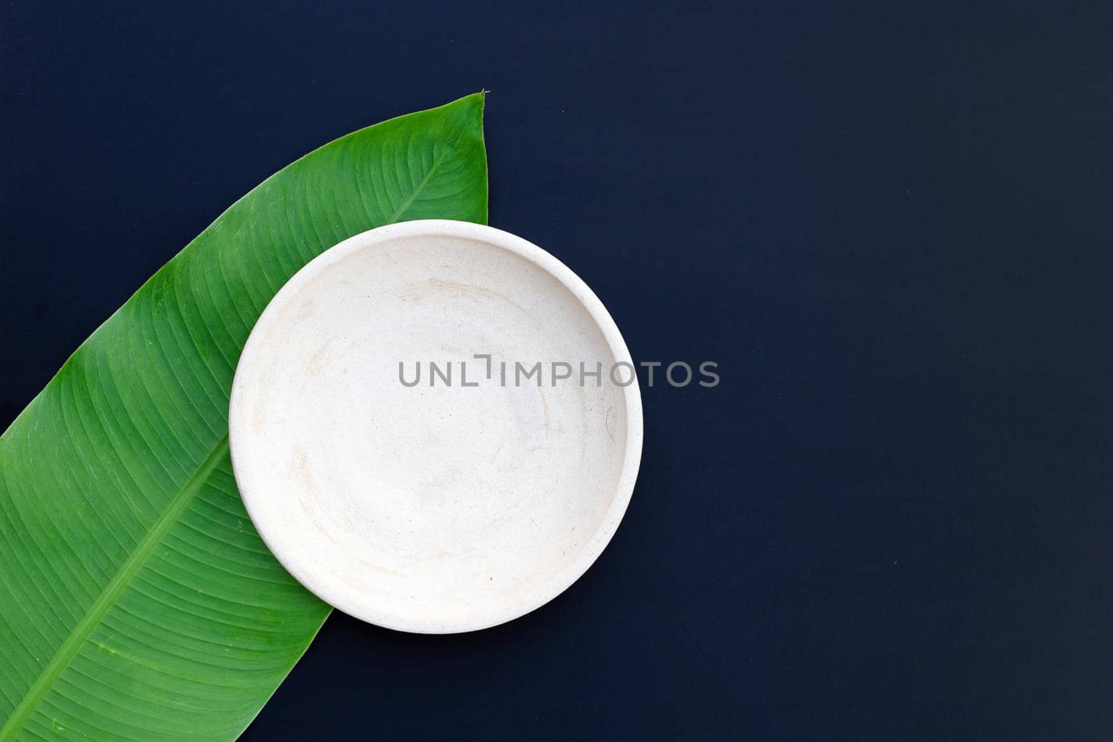 Empty white plate on tropical banana leaves on dark background. Top view
