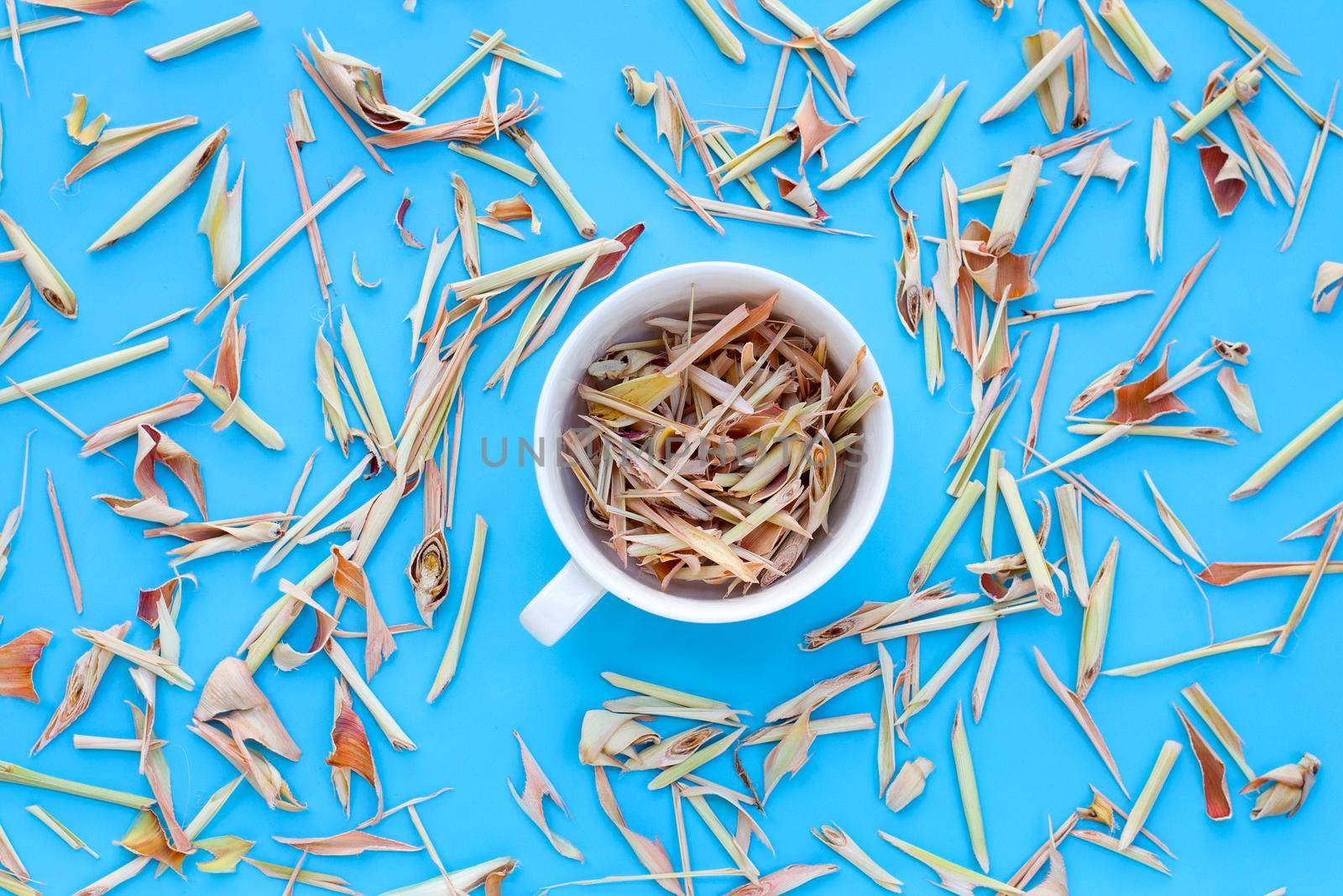 Organic dried lemongrass in white cup on blue background. Herbal tea concept