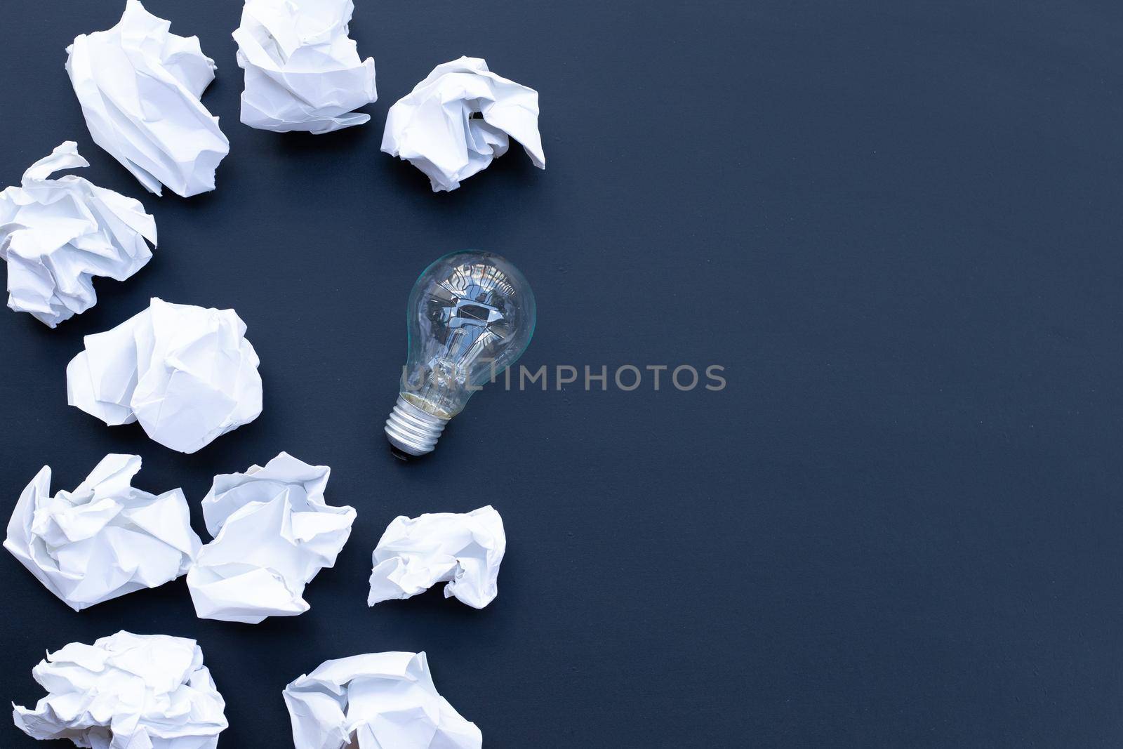Light bulb with white crumpled paper balls on dark background. Ideas and creative thinking concept. Top view by Bowonpat