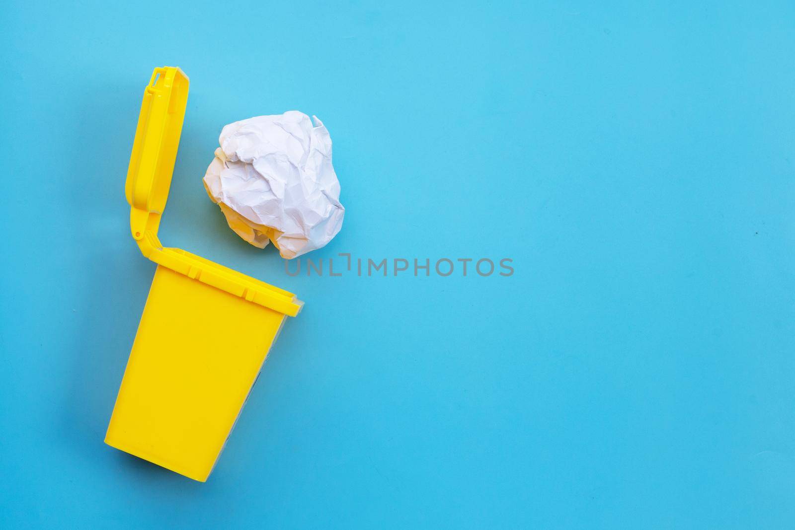 Yellow bin with white crumpled paper on blue background. Ideas and creative thinking concept. Top view by Bowonpat