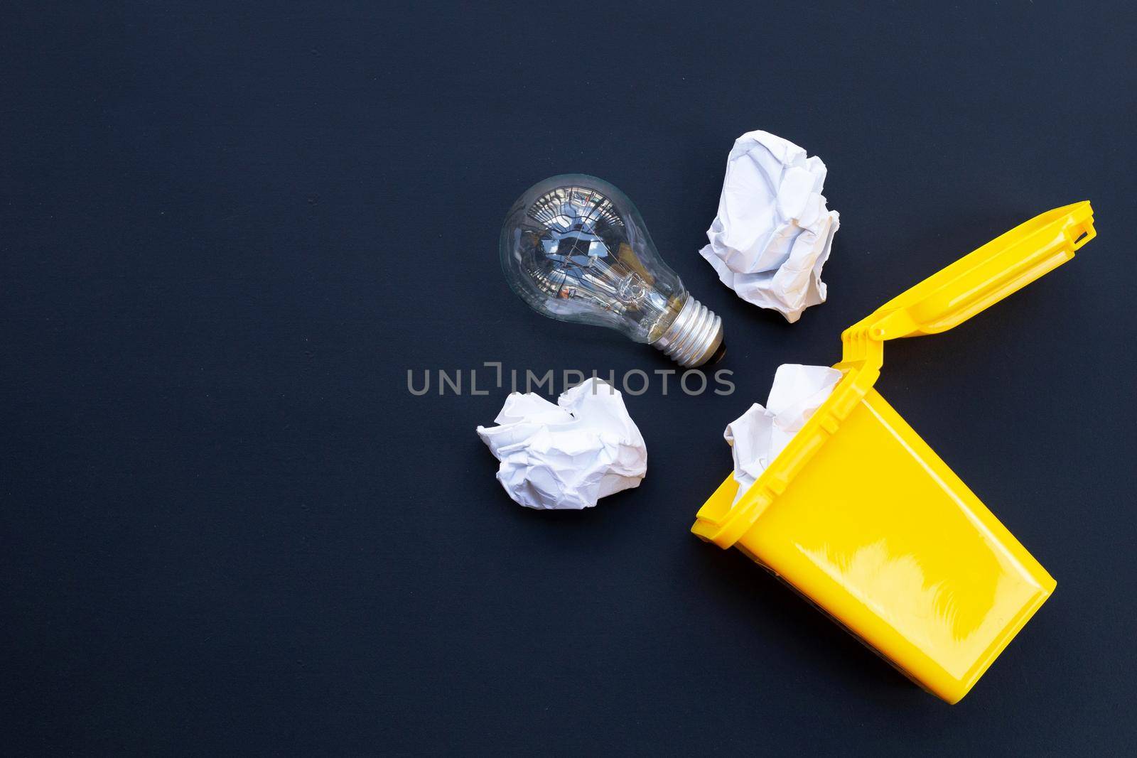 Yellow bin with light bulb and white crumpled paper on dark background. Ideas and creative thinking concept. Top view by Bowonpat