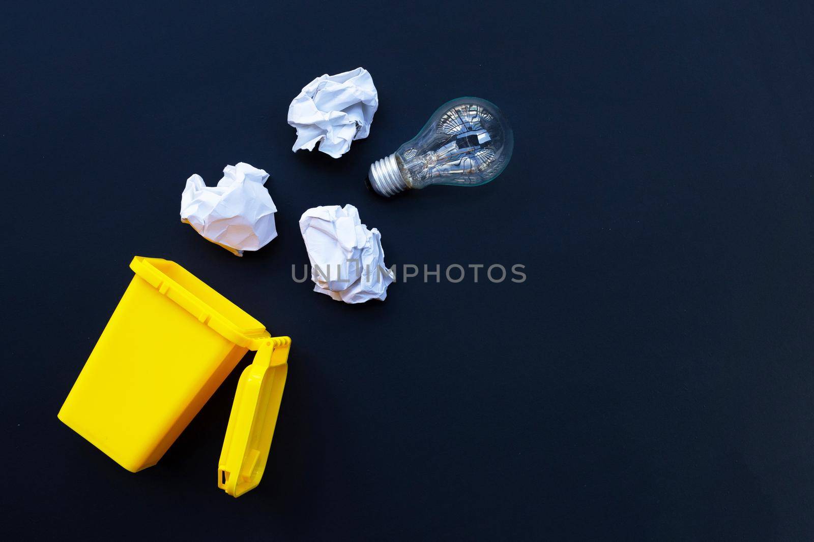 Yellow bin with light bulb and white crumpled paper on dark background. Ideas and creative thinking concept. Top view