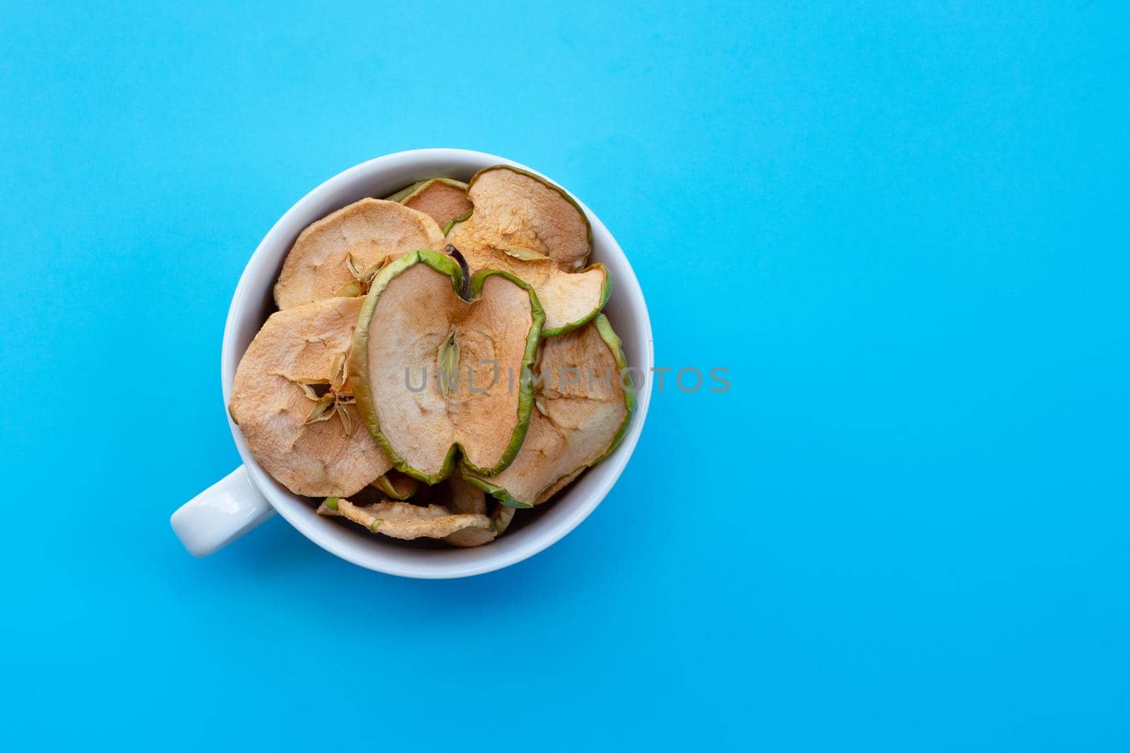 Dried apple slices in white cup on blue background