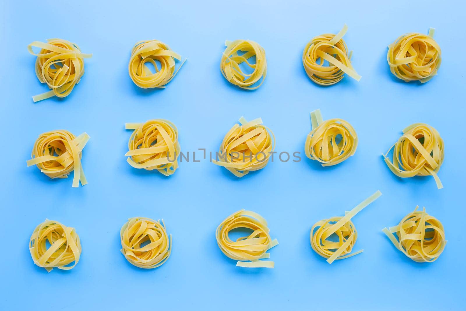 Uncooked Italian pasta tagliatelle nest on blue background. Copy space