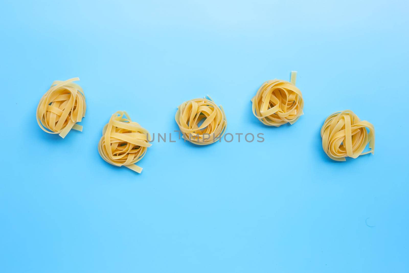 Uncooked Italian pasta tagliatelle nest on blue background. Copy space by Bowonpat