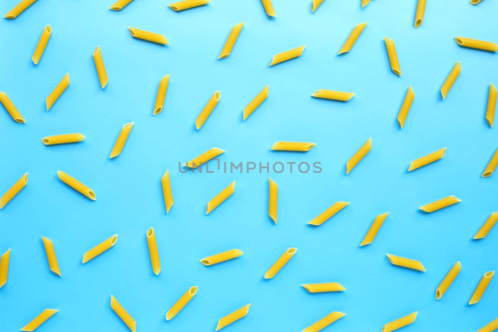Uncooked penne pasta on blue background. Copy space by Bowonpat