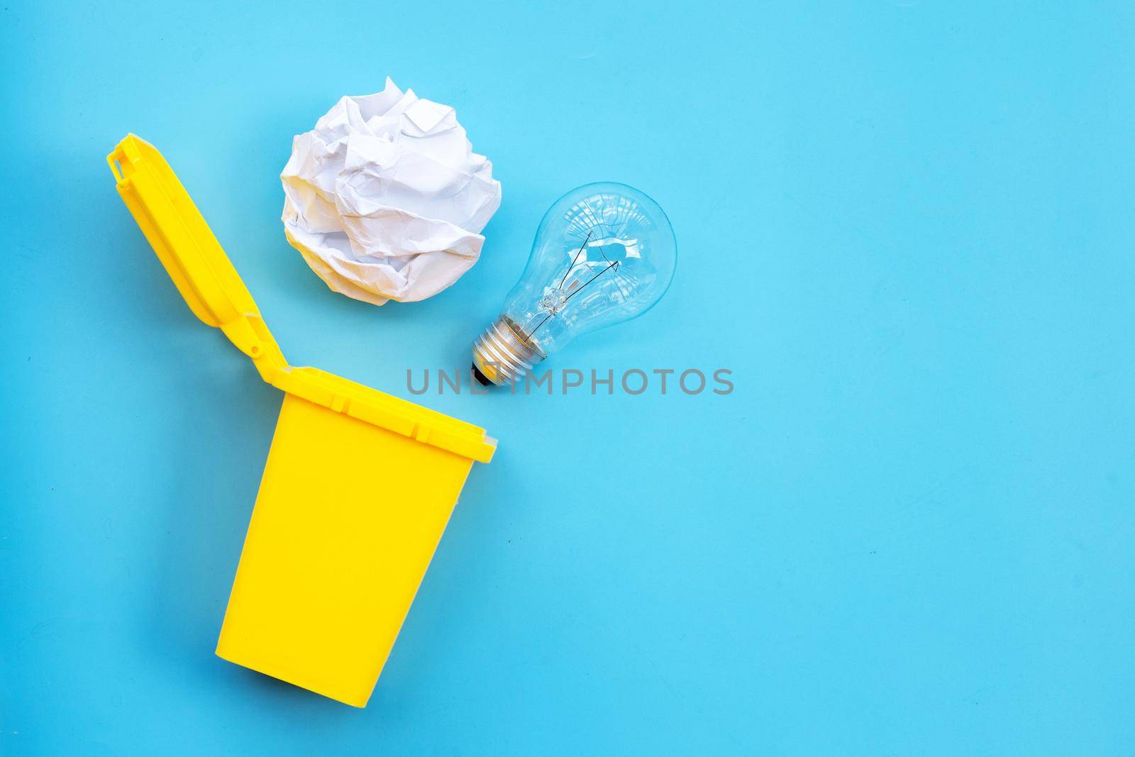 Yellow bin with light bulb and white crumpled paper on blue background. Ideas and creative thinking concept. Top view by Bowonpat
