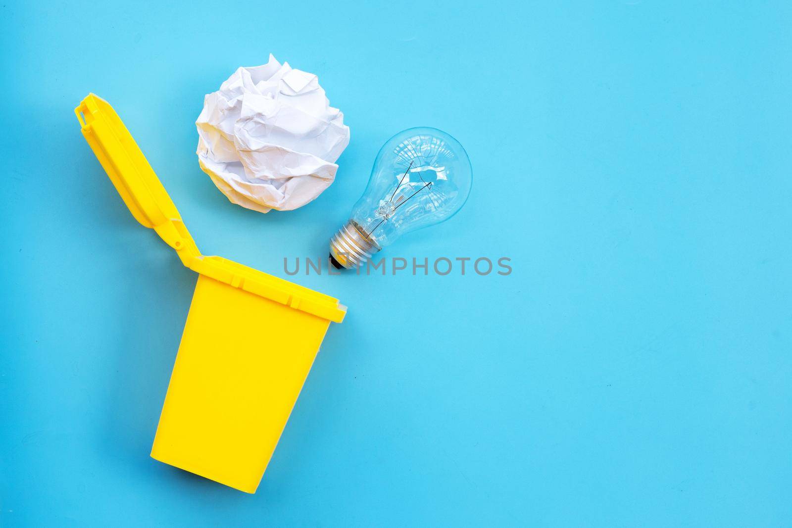 Yellow bin with light bulb and white crumpled paper on blue background. Ideas and creative thinking concept. Top view