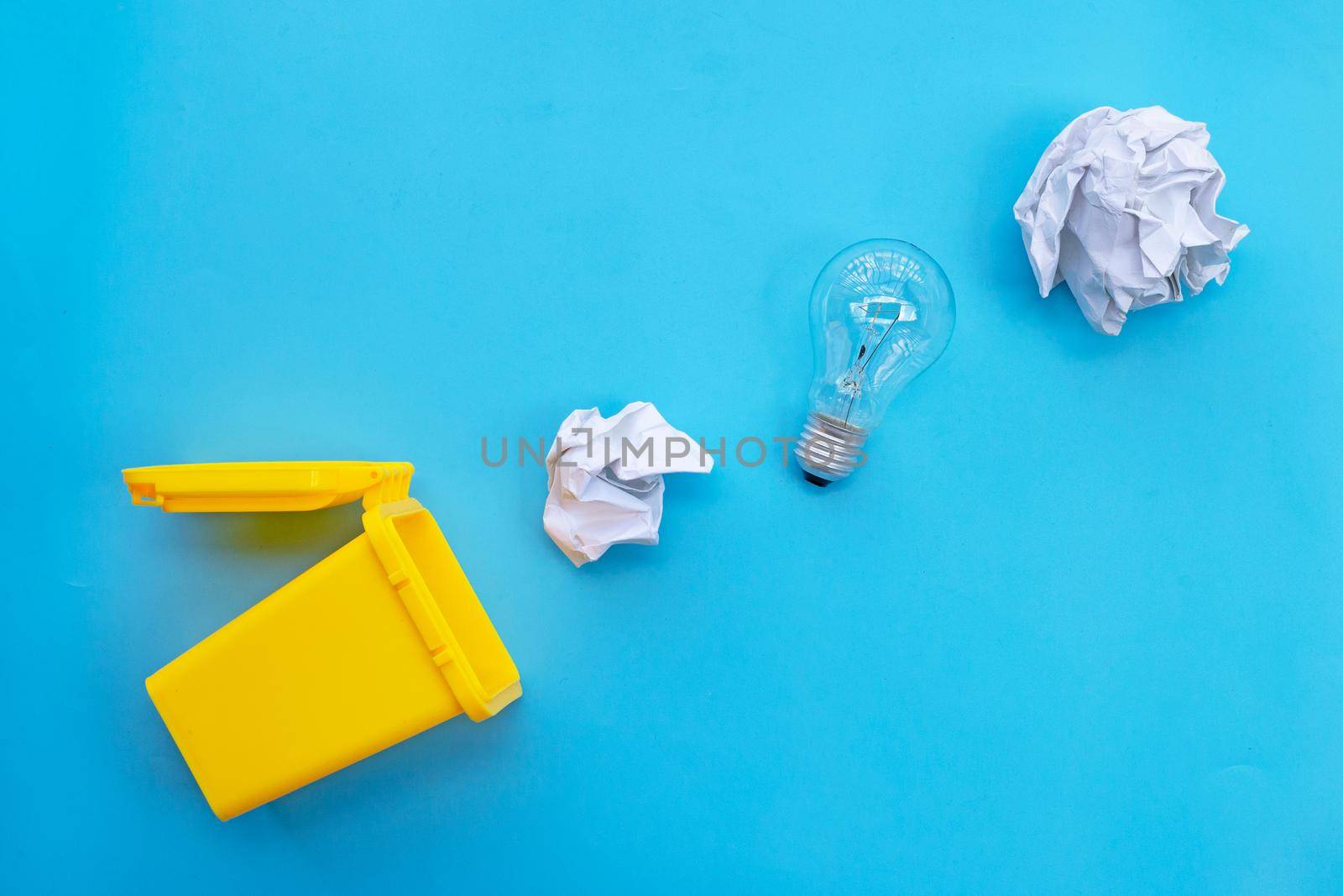 Yellow bin with light bulb and white crumpled paper on blue background. Ideas and creative thinking concept. Top view
