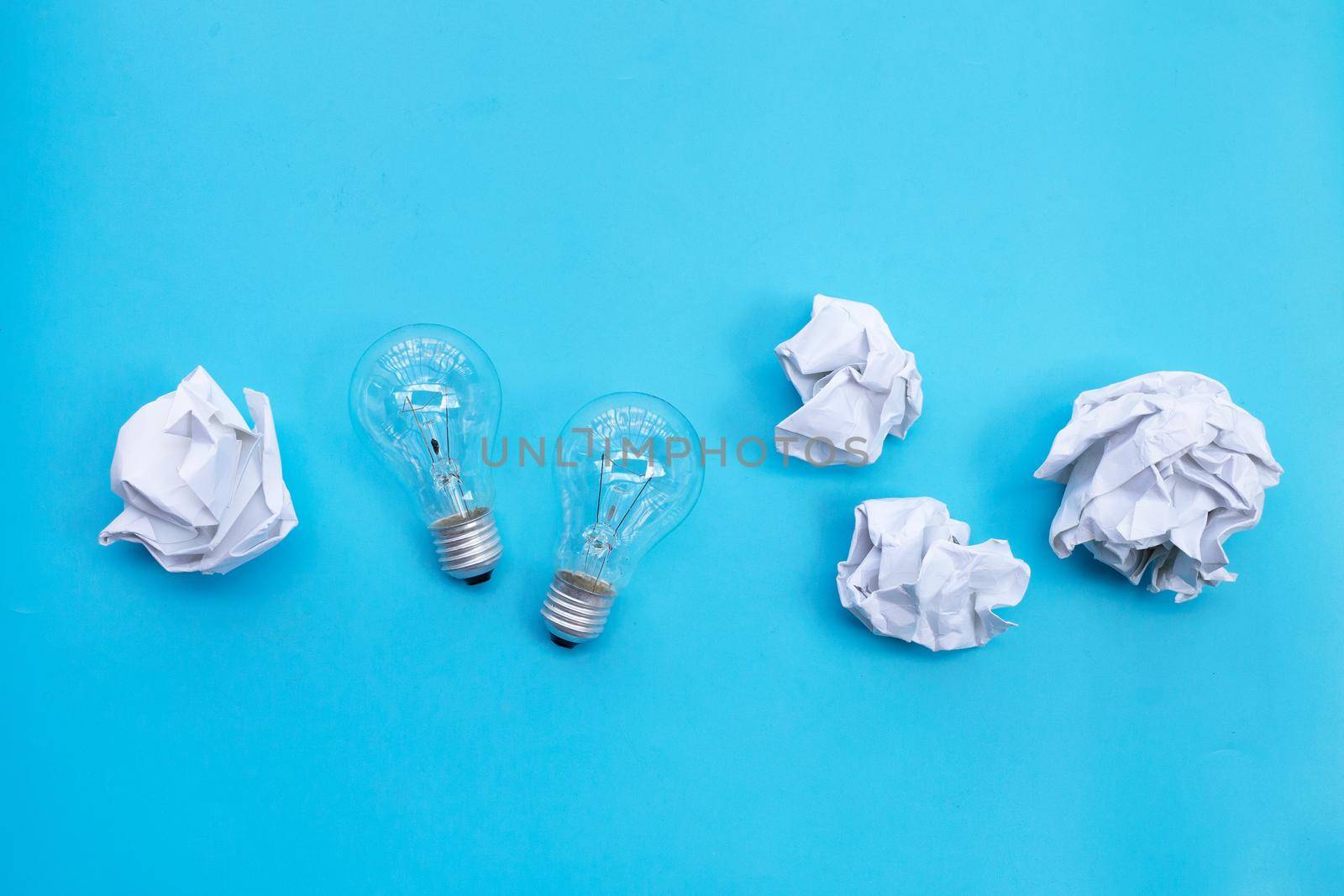 Light bulb with white crumpled paper on blue background. Ideas and creative thinking concept. Top view