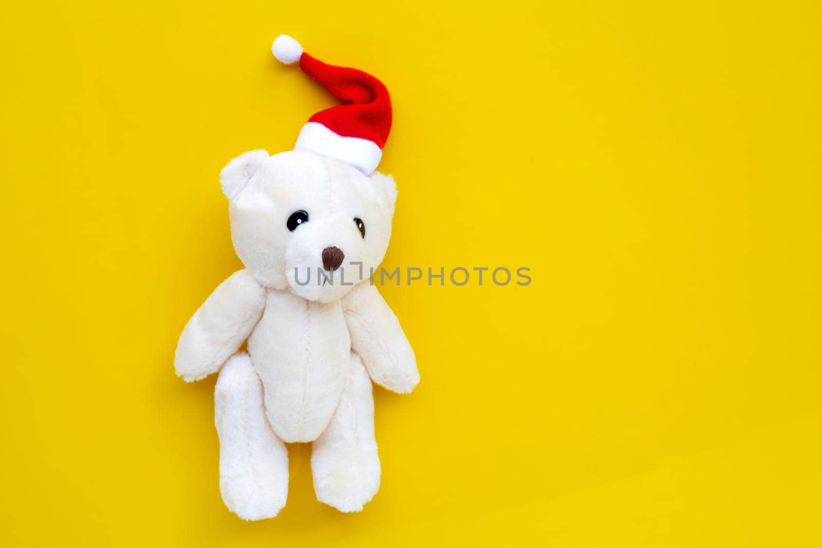 Toy bear wearing a santa hat on yellow background. Christmas holidays concept