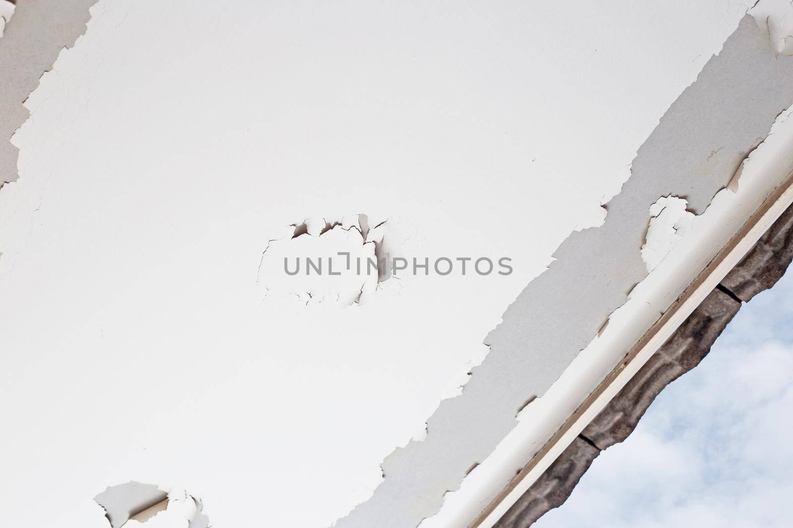 White color paint peeling off on ceiling house. Under the roof