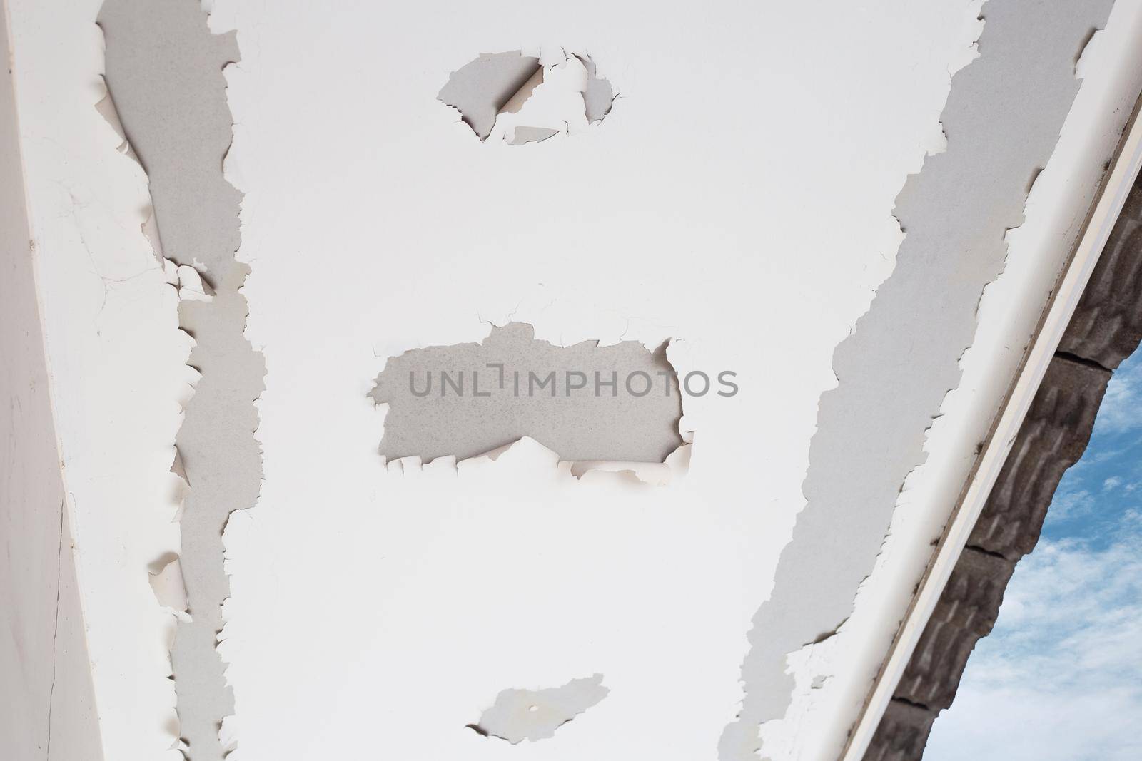 White color paint peeling off on ceiling house. Under the roof
