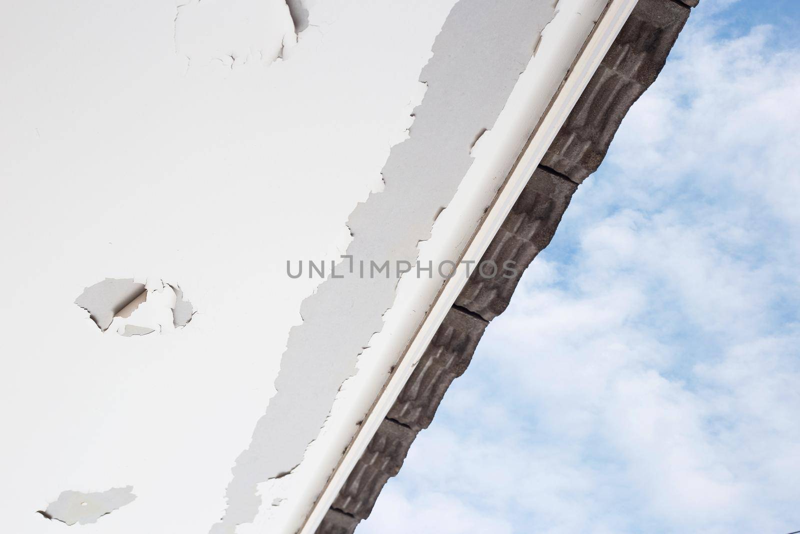 White color paint peeling off on ceiling house. Under the roof