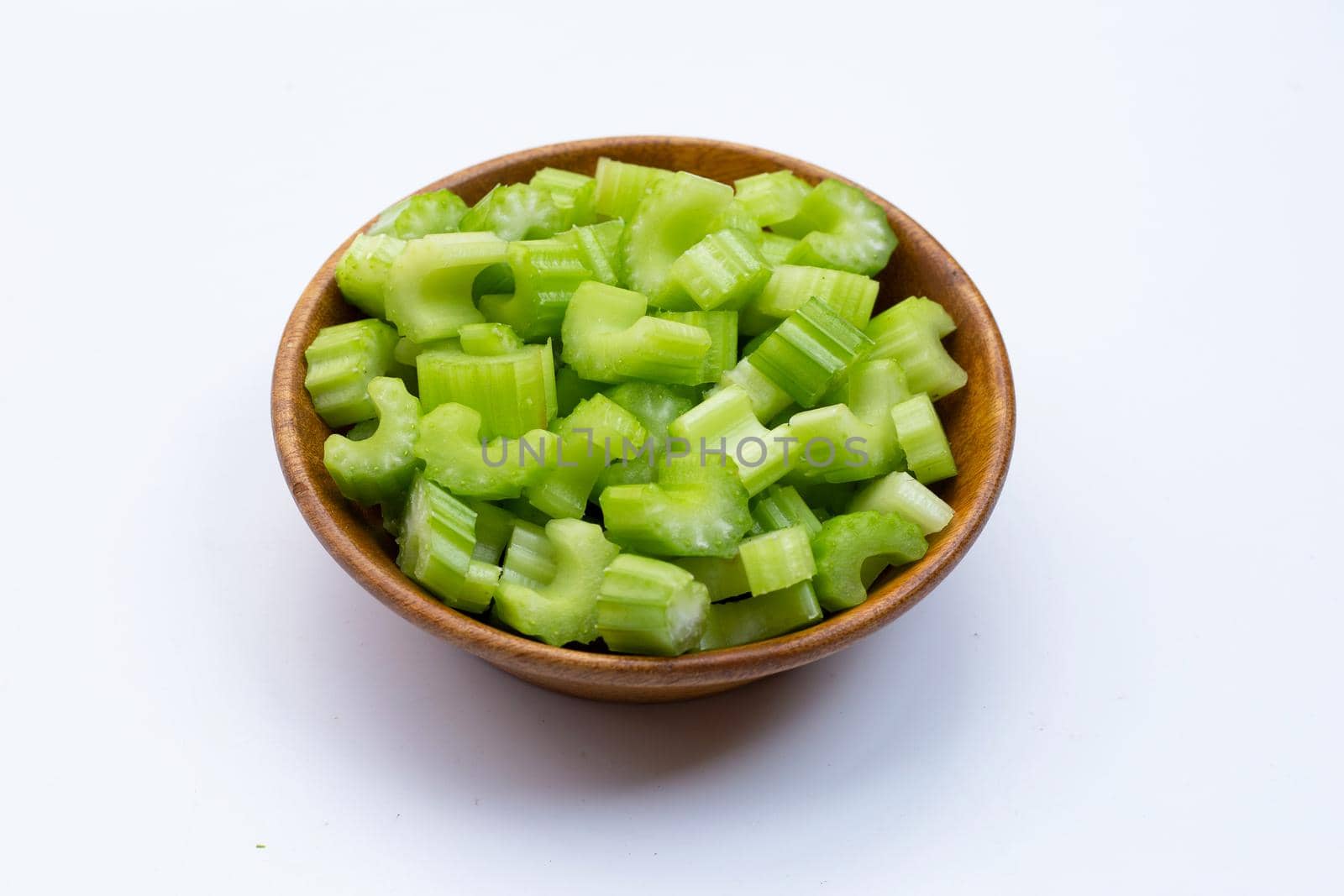 Slices of celery in wooden bowl on white background.