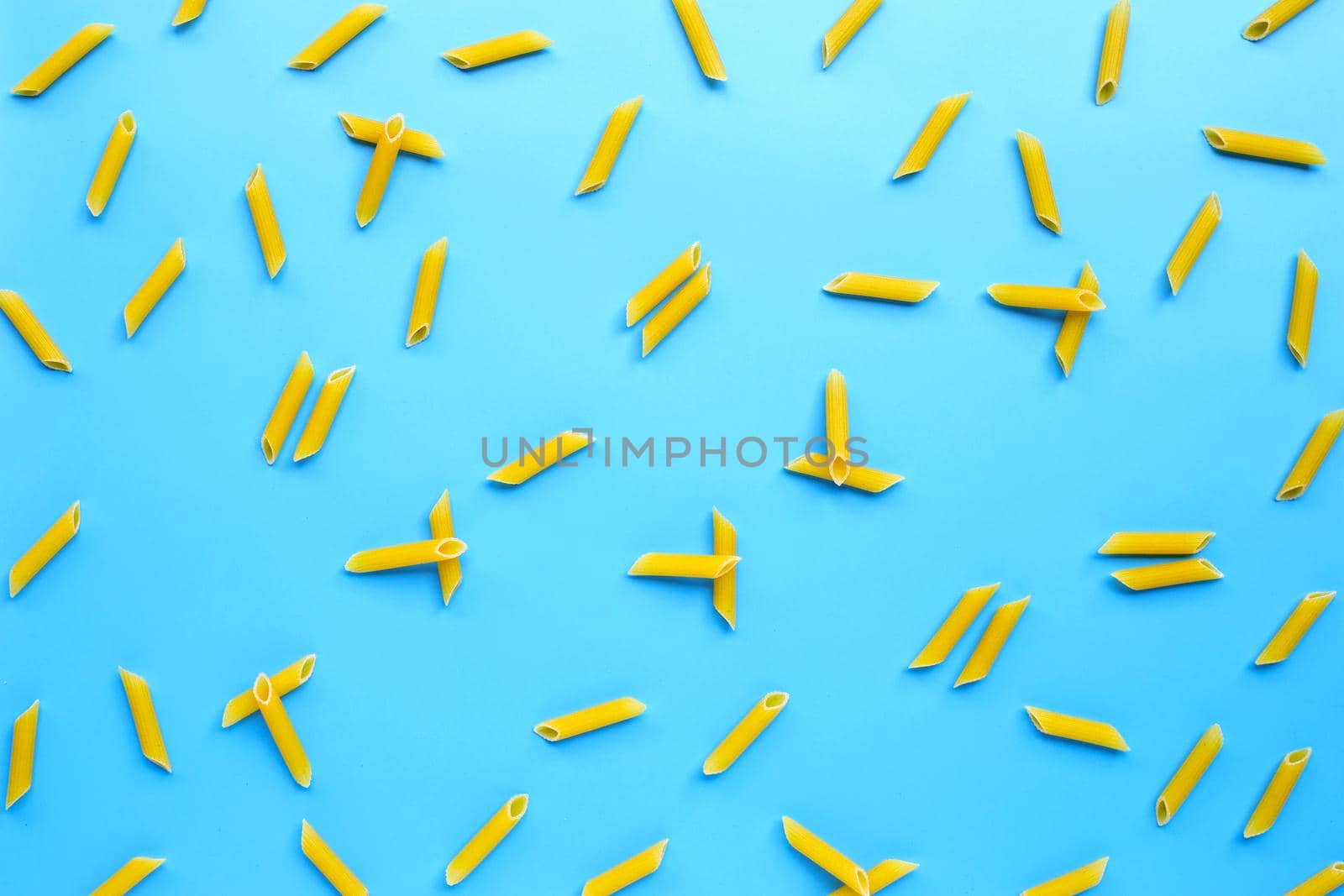 Uncooked penne pasta on blue background. Copy space