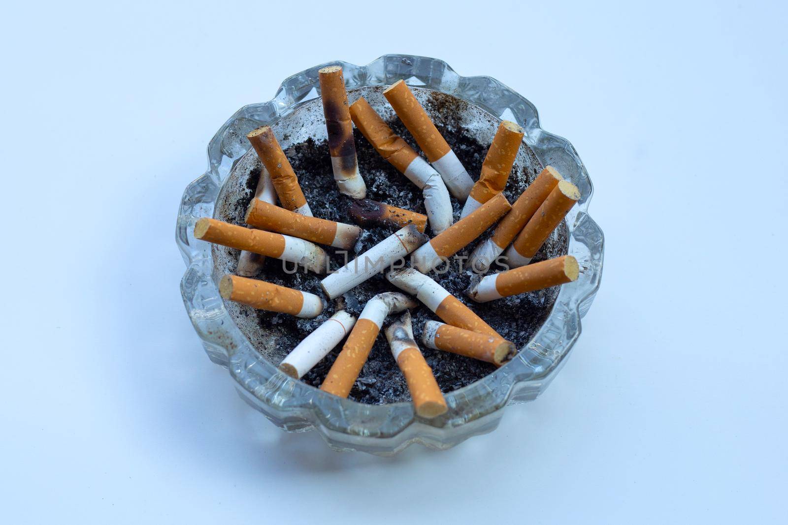 Cigarette butts in glass ashtray on white background.